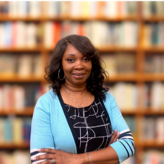 African American female with blue cardigan standing in front of a bookshelf